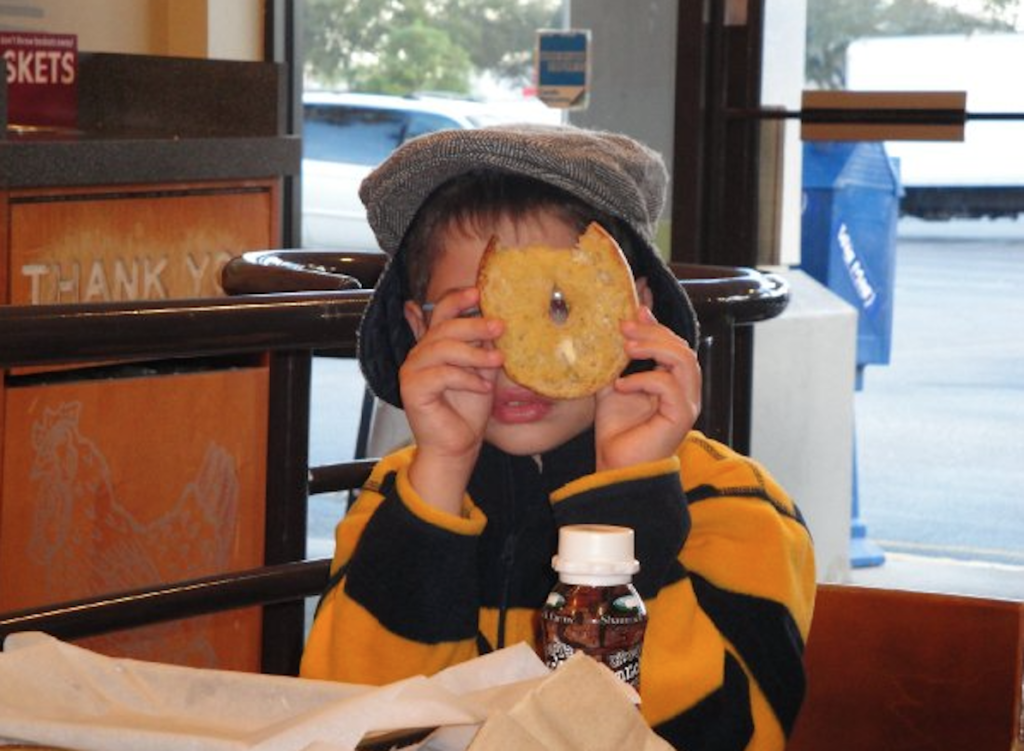 A kid holding a bagel and looking through its hole