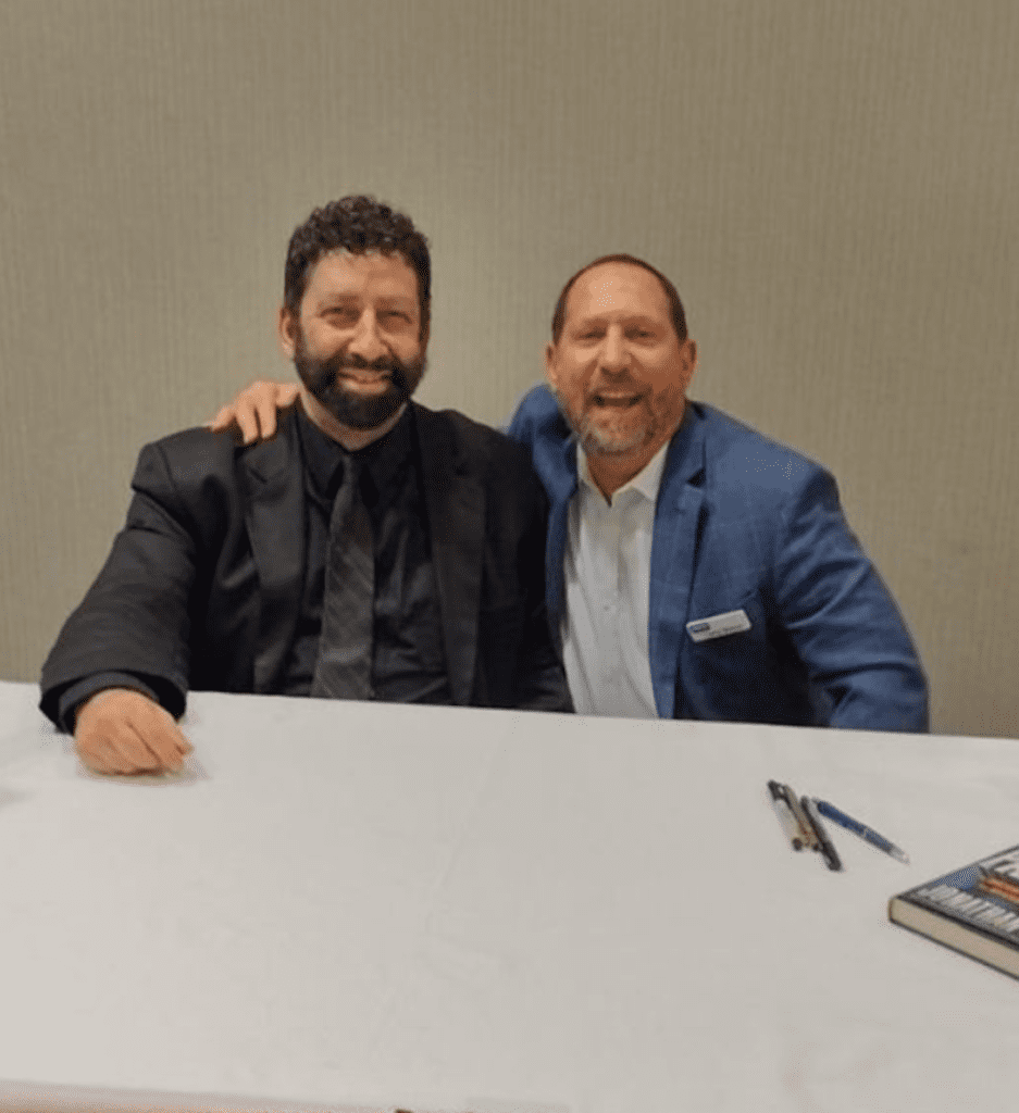 Two people sitting together at a white table wearing suits