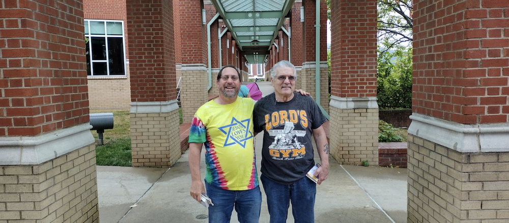 Two men smiling in front of a brick building.