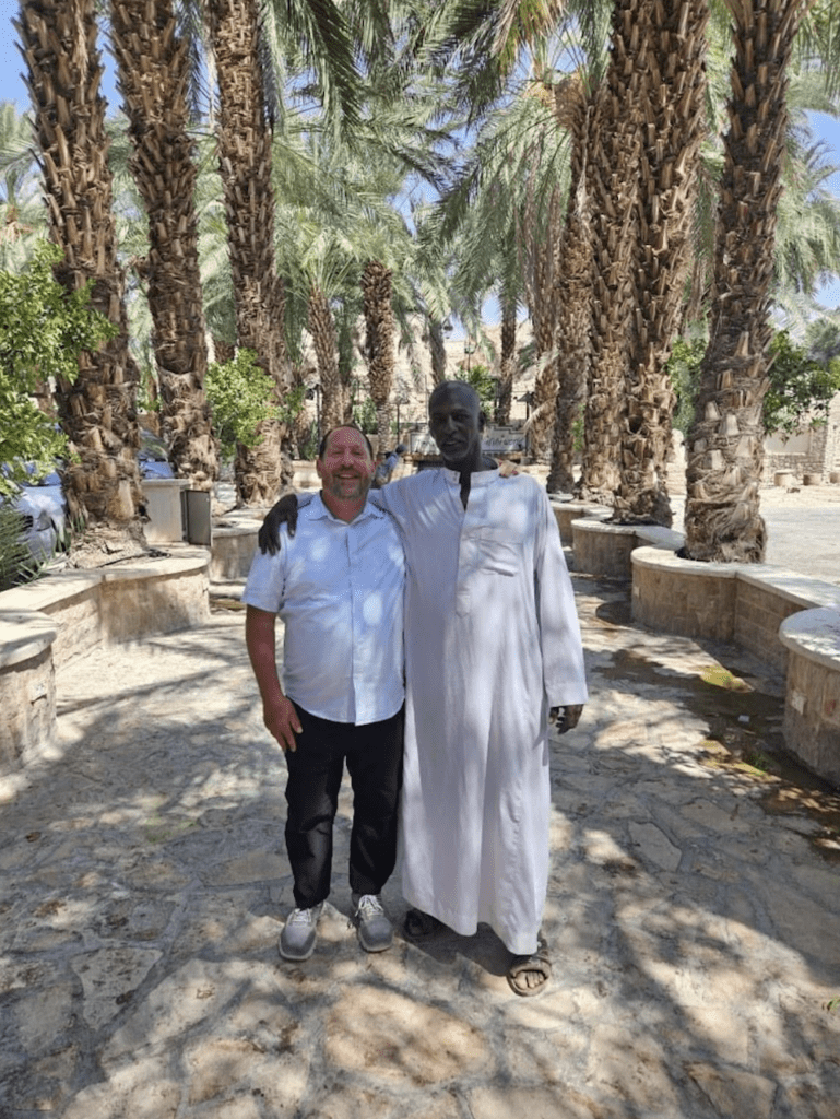 Two men stand together in a palm grove.