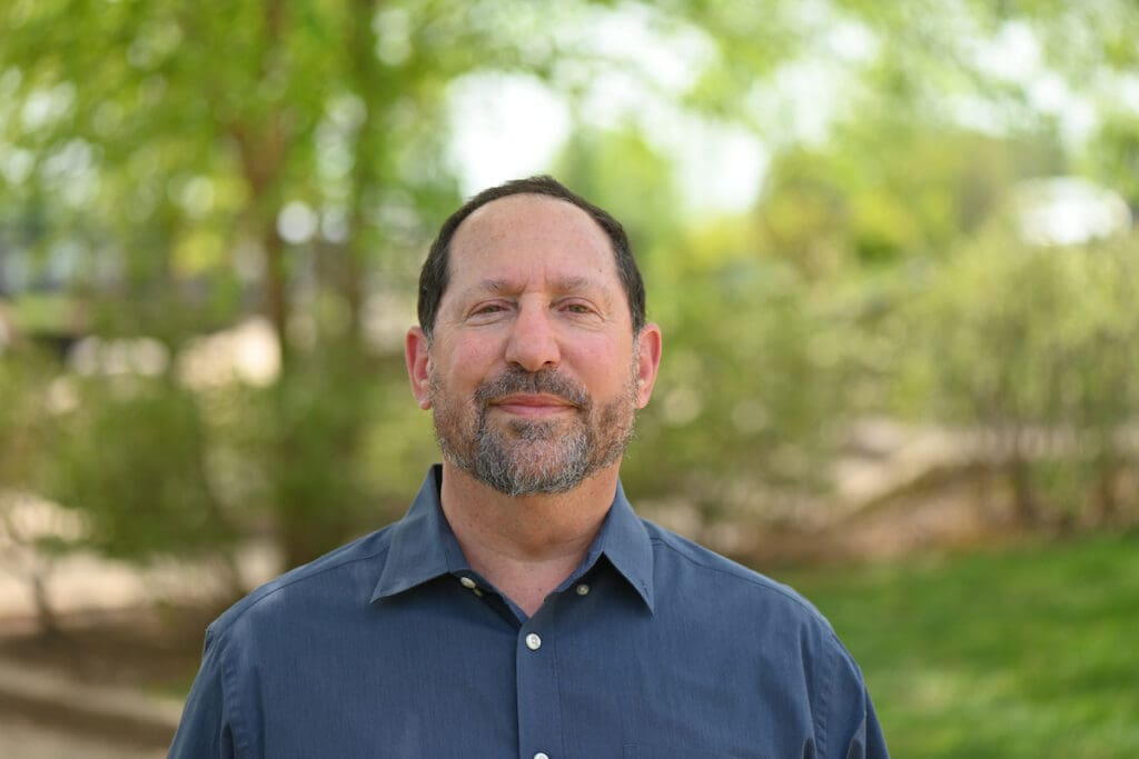 A man smiling in a blue shirt outdoors.