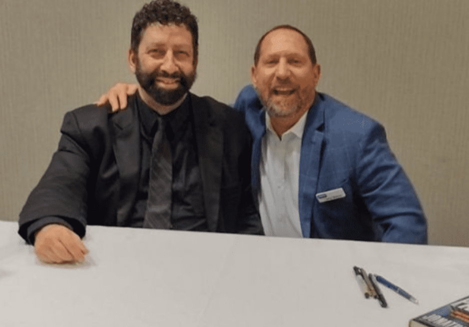 Two people sitting together at a white table wearing suits