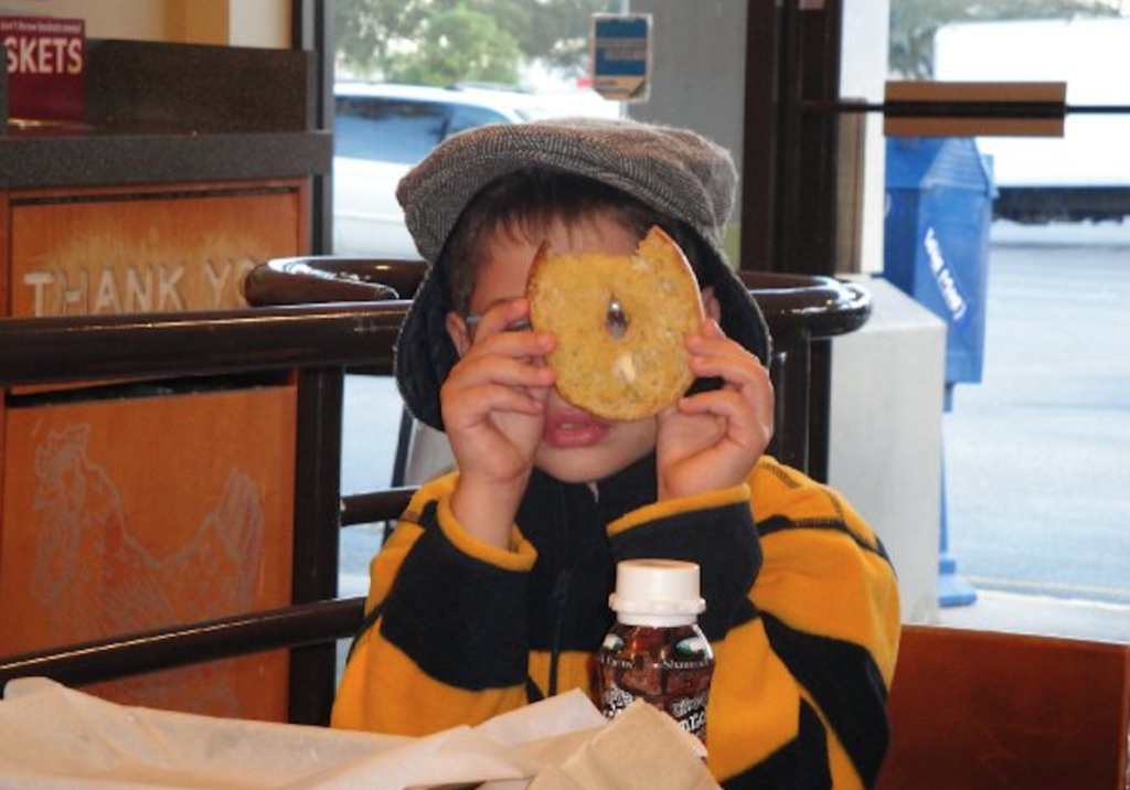 A kid holding a bagel and looking through its hole