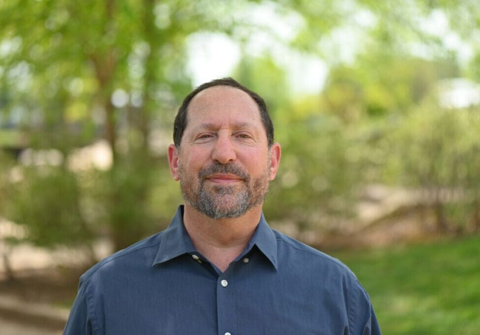 A man smiling in a blue shirt outdoors.